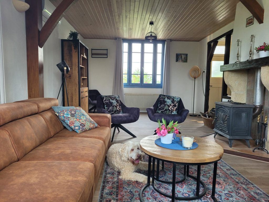 Cozy living room with leather sofa, armchairs, wooden fireplace, floral cushions, and a coffee table with flowers and tea set